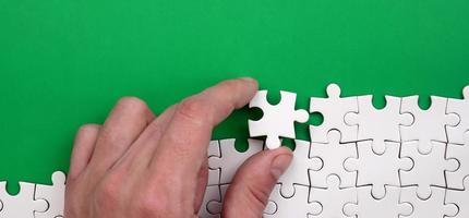 The hand folds a white jigsaw puzzle against the background of the green surface. Texture photo with space for text