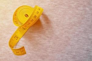 Yellow measuring tape lies on a gray knitted fabric photo