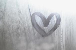 A heart-shaped drawing drawn by a finger on a misted glass in rainy weather photo