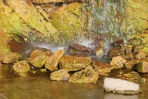 Waterfall among stones and trees. Close-up of boulders in water. Huge stones in green moss. Beautiful landscape of fast waterfall with small whirlpools photo