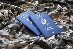 Ukrainian foreign passport on fabric with texture of military pixeled camouflage. Cloth with camo pattern in grey, brown and green pixel shapes and Ukrainian ID photo