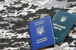 Ukrainian military ID and foreign passport on fabric with texture of pixeled camouflage. Cloth with camo pattern in grey, brown and green shapes with Ukrainian army personal token and passport. photo