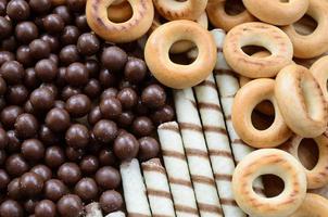 A lot of crispy sweet tubules, chocolate melting balls and yellow bagels lie on a wooden surface. Close up view photo