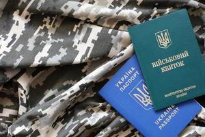 Ukrainian military ID and foreign passport on fabric with texture of pixeled camouflage. Cloth with camo pattern in grey, brown and green shapes with Ukrainian army personal token and passport. photo