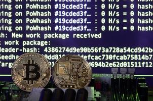 Two bitcoins lies on a videocard surface with background of screen display of cryptocurrency mining by using the GPUs photo