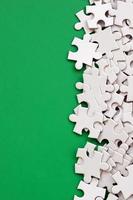 A pile of uncombed elements of a white jigsaw puzzle lies on the background of a green surface. Texture photo with copy space for text