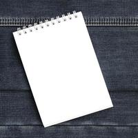 White notebook with clean pages lying on dark blue jeans background. Image with copy space photo