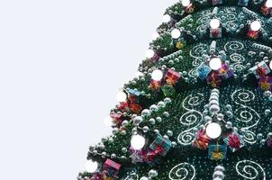 A fragment of a huge Christmas tree with many ornaments, gift boxes and luminous lamps. Photo of a decorated Christmas tree close-up with copy space