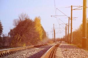 Autumn industrial landscape. Railway receding into the distance among green and yellow autumn trees photo