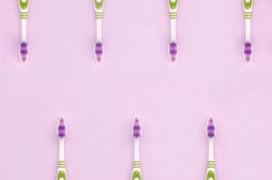 A lot of toothbrushes lie on a pastel pink background photo