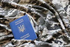 SUMY, UKRAINE - MARCH 20, 2022 Ukrainian foreign passport on fabric with texture of military pixeled camouflage. Cloth with camo pattern in grey, brown and green pixel shapes and Ukrainian ID photo