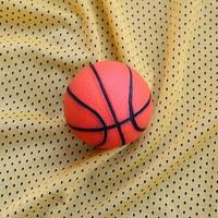 el pequeño baloncesto de goma naranja se encuentra sobre una textura de tela de jersey deportivo amarillo y un fondo con muchos pliegues foto