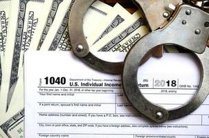 Police handcuffs lie on the tax form 1040. The concept of problems with the law in the aftermath of non-payment of taxes photo