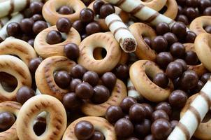 A lot of crispy sweet tubules, chocolate melting balls and yellow bagels lie on a wooden surface. Close up view photo