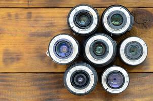 Several photographic lenses lie on a brown wooden background. Space for text photo