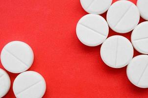 A few white tablets lie on a bright red background surface. Background image on medical and pharmaceutical topics photo