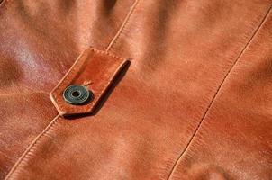 Brown leather texture. Useful as background for any design work. Macro photo of a button on outer clothing made of genuine leather