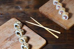 A detailed shot of a set of Japanese sushi rolls and a device for their use chopsticks , which are located on a wooden cutting board on a table in the kitchen of a sushi bar photo