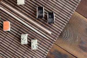 Sushi rolls and wooden chopsticks lie on a bamboo straw serwing mat. Traditional Asian food. Top view photo