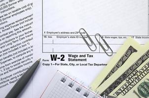 The pen, notebook and dollar bills is lies on the tax form W-2 Wage and Tax Statement. The time to pay taxes photo