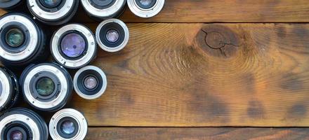 Several photographic lenses lie on a brown wooden background. Space for text photo