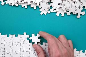 The hand folds a white jigsaw puzzle and a pile of uncombed puzzle pieces lies against the background of the blue surface. Texture photo with space for text