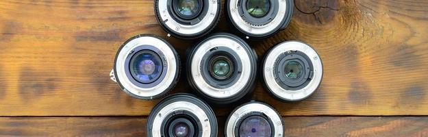 Several photographic lenses lie on a brown wooden background. Space for text photo