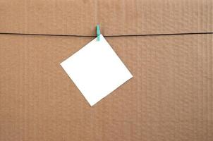 White blank card on rope on a brown cardboard background. Creative reminder, small sheet of paper on wooden clothespin, memo backdrop photo