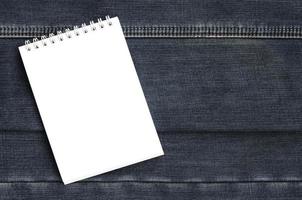 White notebook with clean pages lying on dark blue jeans background. Image with copy space photo