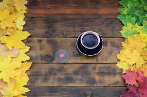 una taza de té y un hilandero de madera entre las muchas hojas de otoño caídas amarillentas en la superficie de fondo hechas de tablas de madera natural de color marrón oscuro foto