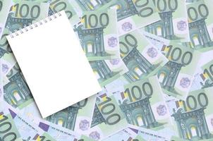 White notebook with clean pages lying on a set of green monetary denominations of 100 euros. A lot of money forms an infinite heap photo