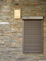 A window with brown metal rolling shutters and wall decoration with artificial stone photo