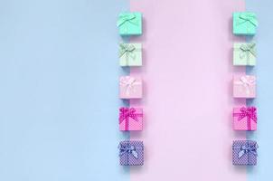 Small gift boxes of different colors with ribbons lies on a violet and pink background photo