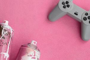 Teenagers and youth lifestyle concept. Joystick and two spray cans lies on the blanket of furry pink fleece fabric. Controllers for video games and paint cans on a plush fleece material background photo