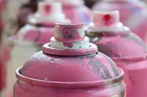 A lot of dirty and used aerosol cans of bright pink paint. Macro photograph with shallow depth of field. Selective focus on the spray nozzle photo