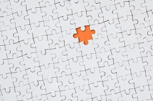 The texture of a white jigsaw puzzle in an assembled state with one missing element forming an orange space photo