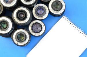 Several photographic lenses and white notebook lie on a bright blue background. Space for text photo