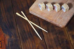 una toma detallada de un conjunto de rollos de sushi japoneses y un dispositivo para su uso, que se encuentran en una tabla de corte de madera sobre una mesa en la cocina de un bar de sushi foto