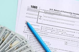 1065 tax form lies near hundred dollar bills and blue pen on a light blue background. US Return for parentship income photo