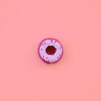 Single small plastic donut lies on a pastel colorful background. Flat lay minimal composition. Top view photo