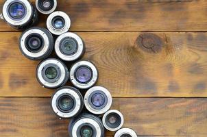 Several photographic lenses lie on a brown wooden background. Space for text photo