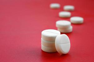 A few white tablets lie on a bright red background surface. Background image on medical and pharmaceutical topics photo