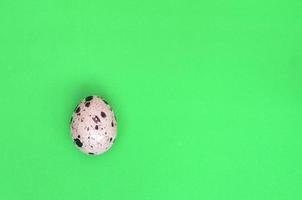 One quail egg on a light green surface, top view, empty place fo photo