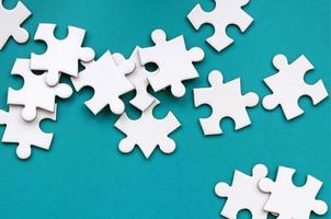 A pile of uncombed elements of a white jigsaw puzzle lies on the background of a green surface. Texture photo with copy space for text