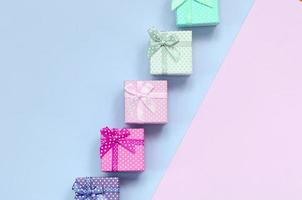 Small gift boxes of different colors with ribbons lies on a violet and pink background photo