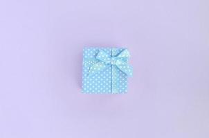 Small blue gift box with ribbon lies on a violet background. Minimalism flat lay top view photo