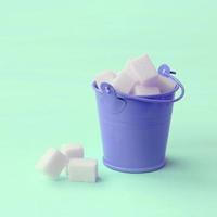 A miniature lilac bucket filled with cubes of sugar lies on a turquoise pastel background photo