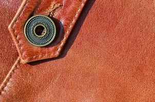 Brown leather texture. Useful as background for any design work. Macro photo of a button on outer clothing made of genuine leather