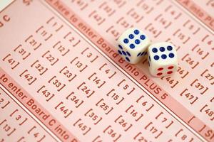 Dice cubes lies on pink gambling sheets with numbers for marking to play lottery. Lottery playing concept or gambling addiction. Close up photo