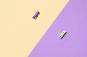 Two colored wooden pegs and small rope lie on texture background of fashion pastel yellow and violet colors photo